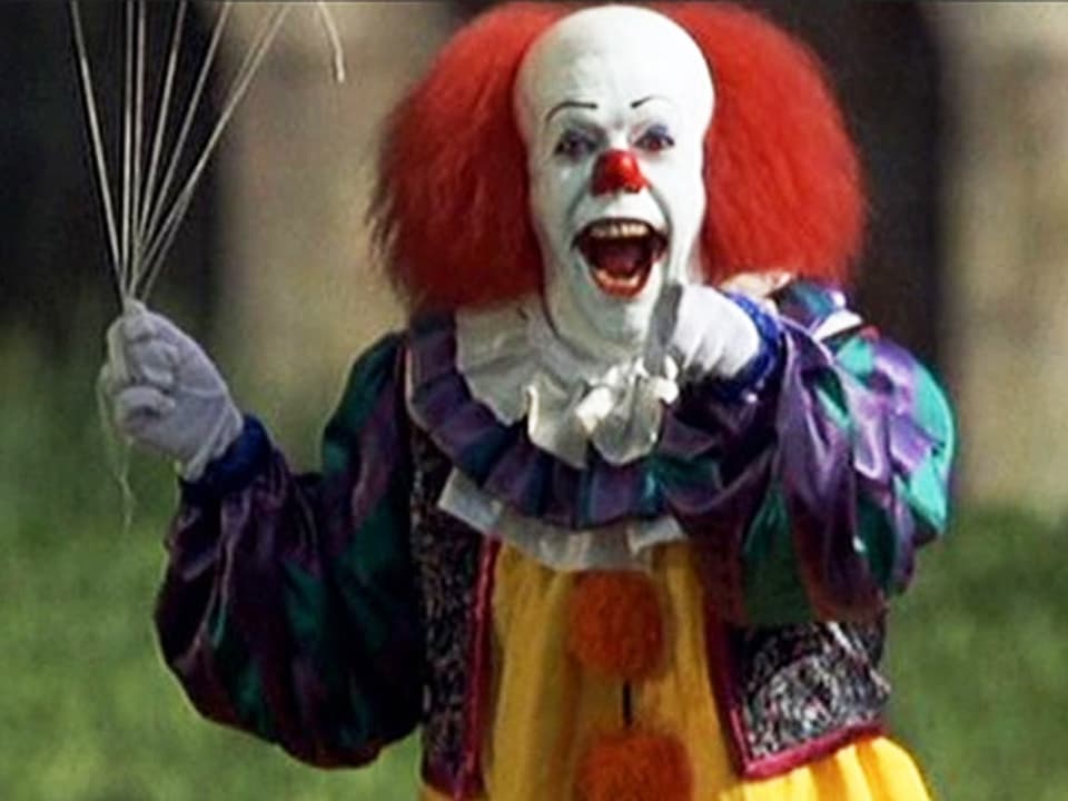 Filmszene: Clown mit weis geschminktem Gesicht, roter Nase und roten Haaren schaut lachend in die Kamera.