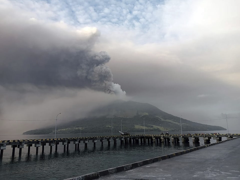 Vulkanasche steigt über einem Berg neben einem Pier auf.