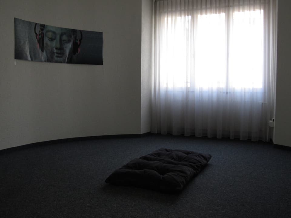 Raum mit Kissen auf Teppich und Poster mit Buddha-Statue. 