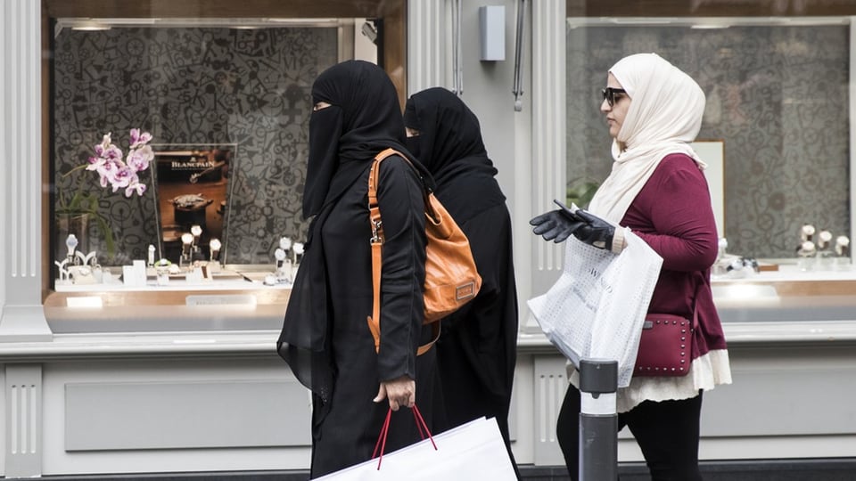 Zwei Frauen in Burka und eine mit Kopftuch gehen mit Einkaufstaschen auf dem Trottoir.