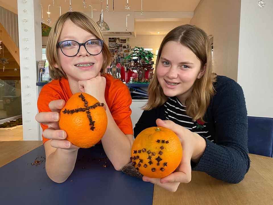 Tiuri und Ronja halten beide Orangen in die Kamera, die sie mit Nägeli in Form eines Kreuzes und eines Velos verzierten.
