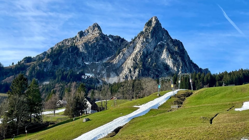 Skilift mit weissem Schneeband in grüner Landschaft.