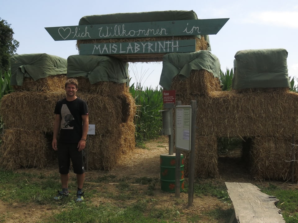 Samuel Mathis steht vor dem Eingang des Maislabyrinths. Auf dem Schild sthet «Herzlich willkommen im Maislabyrinth»