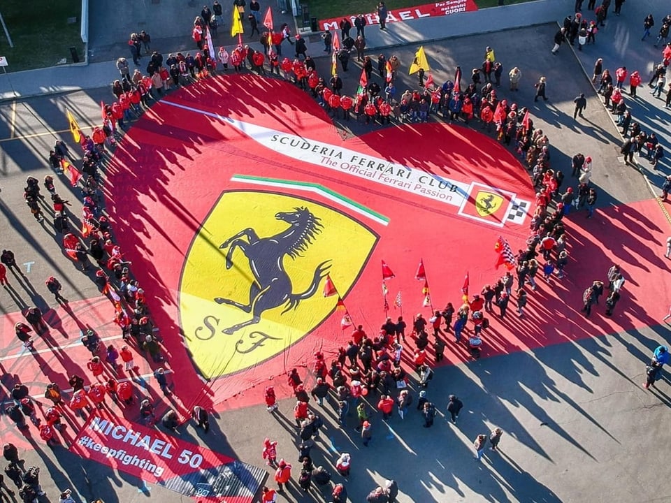 Ein riesiges Ferrari-Herz um das viele Menschen mit Fahnen stehen.