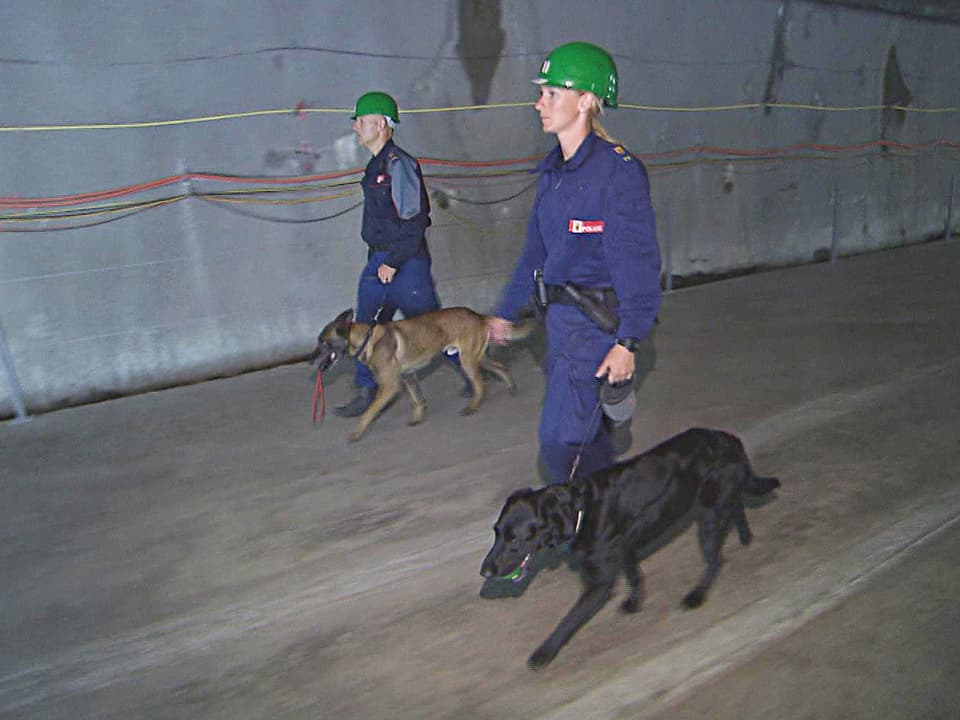 Zwei Polizisten laufen mit den Hunden durch den Tunnel.