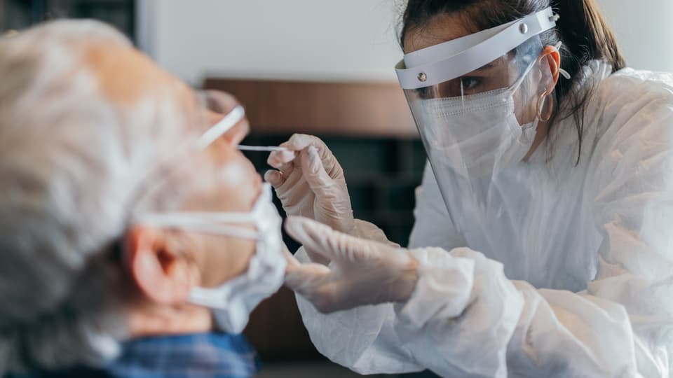 Eine Ärztin schiebt einem Senioren ein Teststäbchen in die Nase.