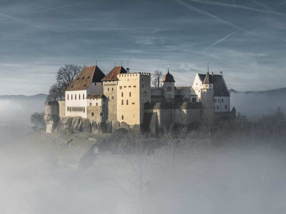 Lenzburg/AG Hügel mit einigen Häusern eines Schlosses ragt aus dem Nebelmeer. Darüber sonnig.