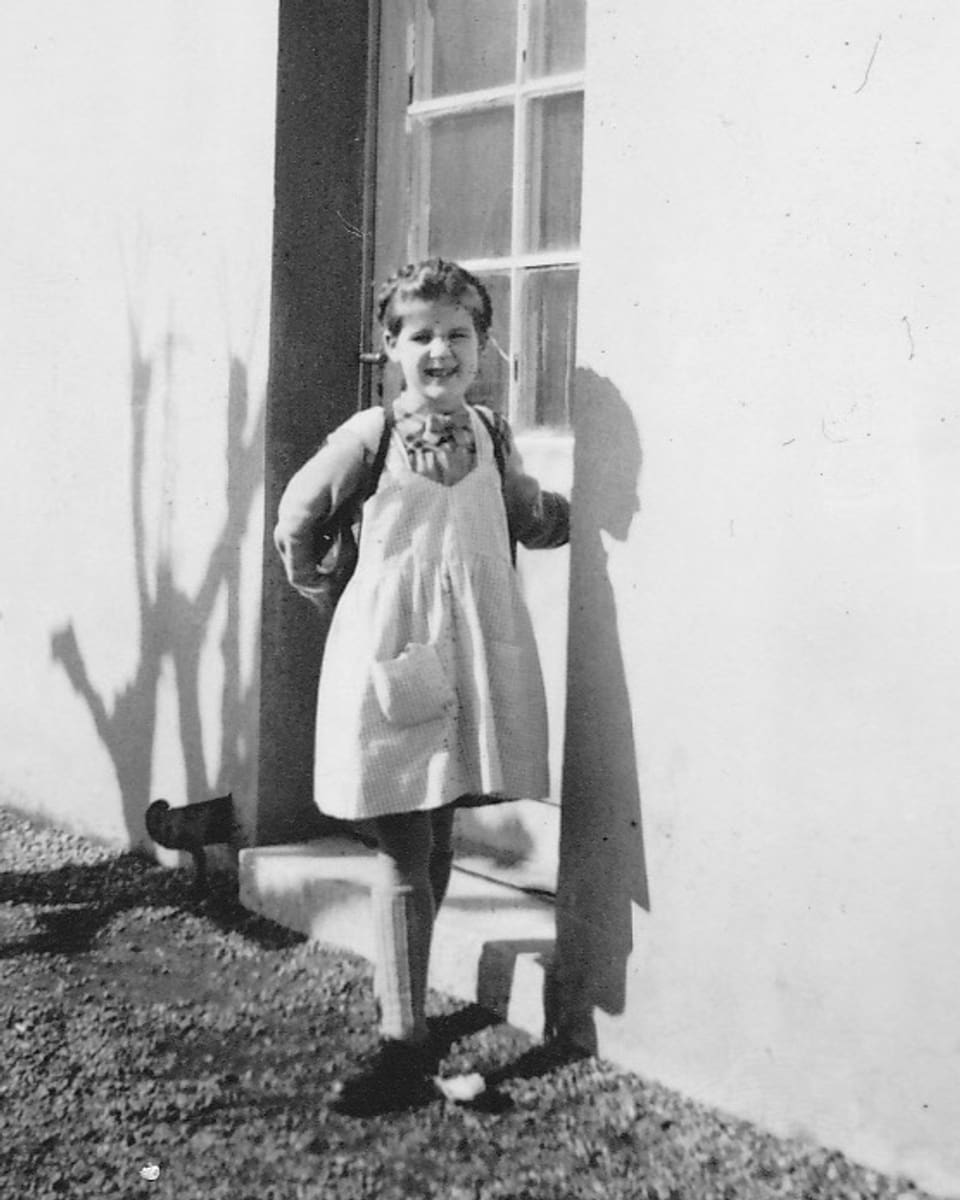 Ein kleines Mädchen steht lachend vor einem Hauseingang.