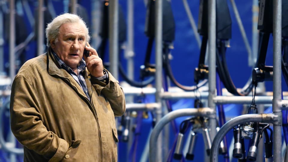 Gérard Depardieu telefoniert vor einer grossen Melkmaschine.