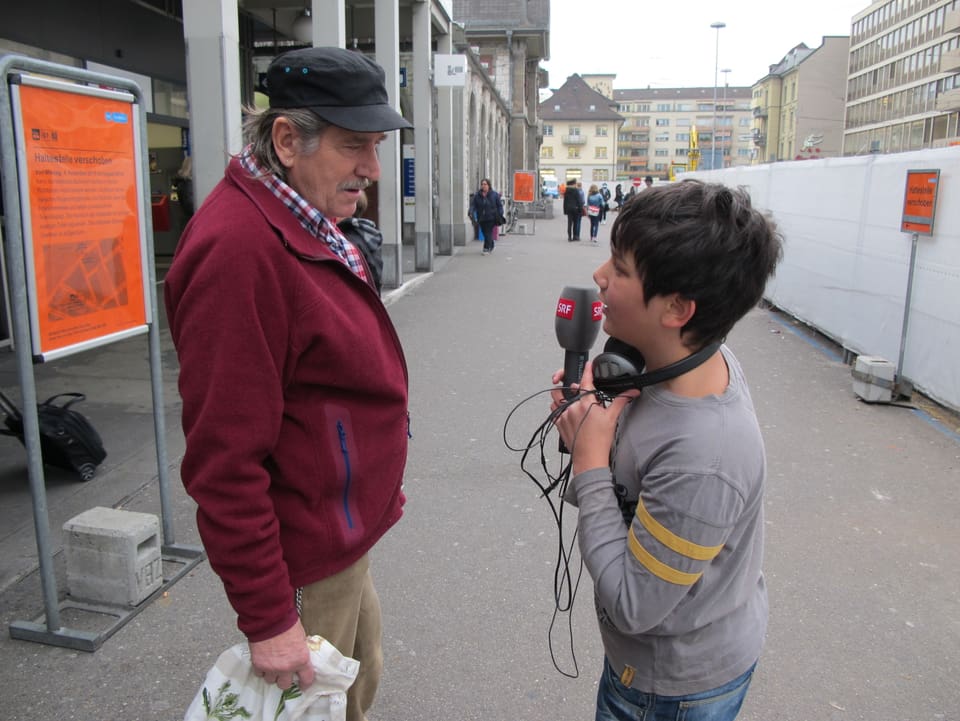 Junge interviewt auf der Strasse einen Passanten. 