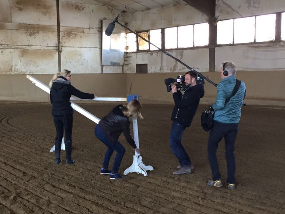 Zwei Frauen richten ein Hindernis für Pferde ein, daneben stehen ein Kameramann und ein Tonoperateur, die die Szene einfangen.