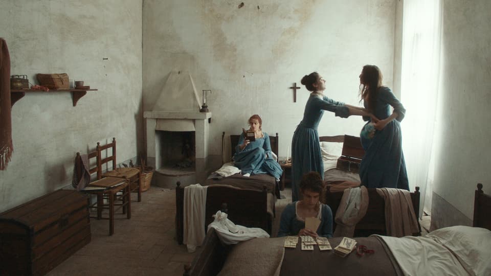 Mädchen in barocken Kostümen verbringen ihre Freizeit mit Kartenspielen, Lesen und Tanzen in einem simplen Schlafzimmer.