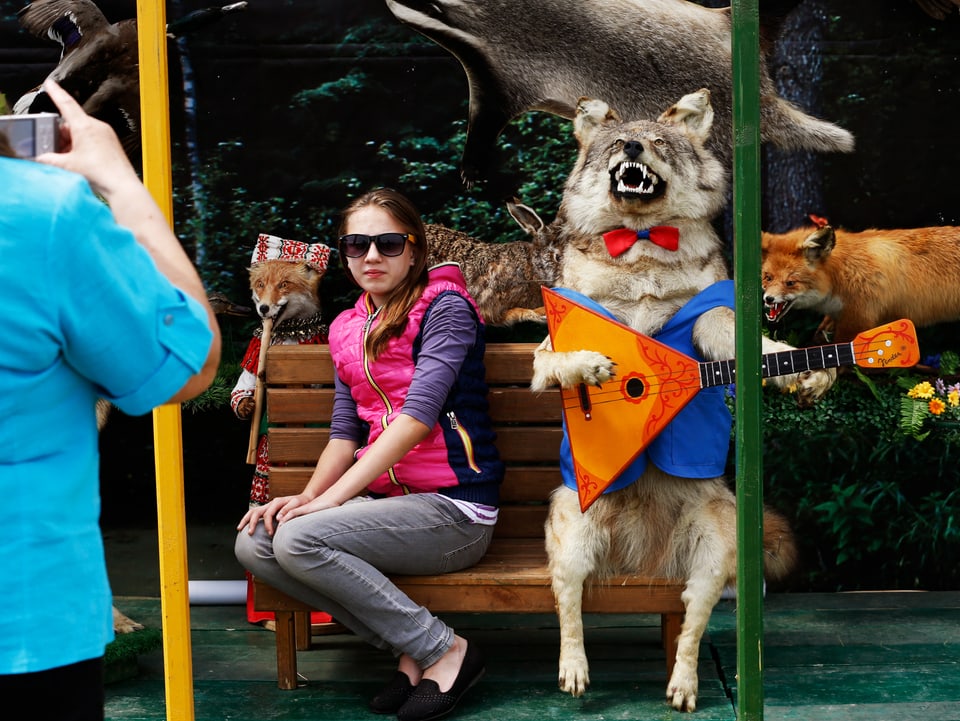 Eine Frau lässt sich mit einem ausgestopften Wolf mit Fliege und Weste, der Laute spielt, fotografieren.
