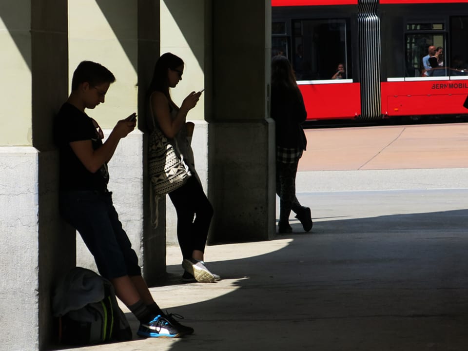Zwei Teenager stehen in einer Laube und schauen auf ihr Smartphone.