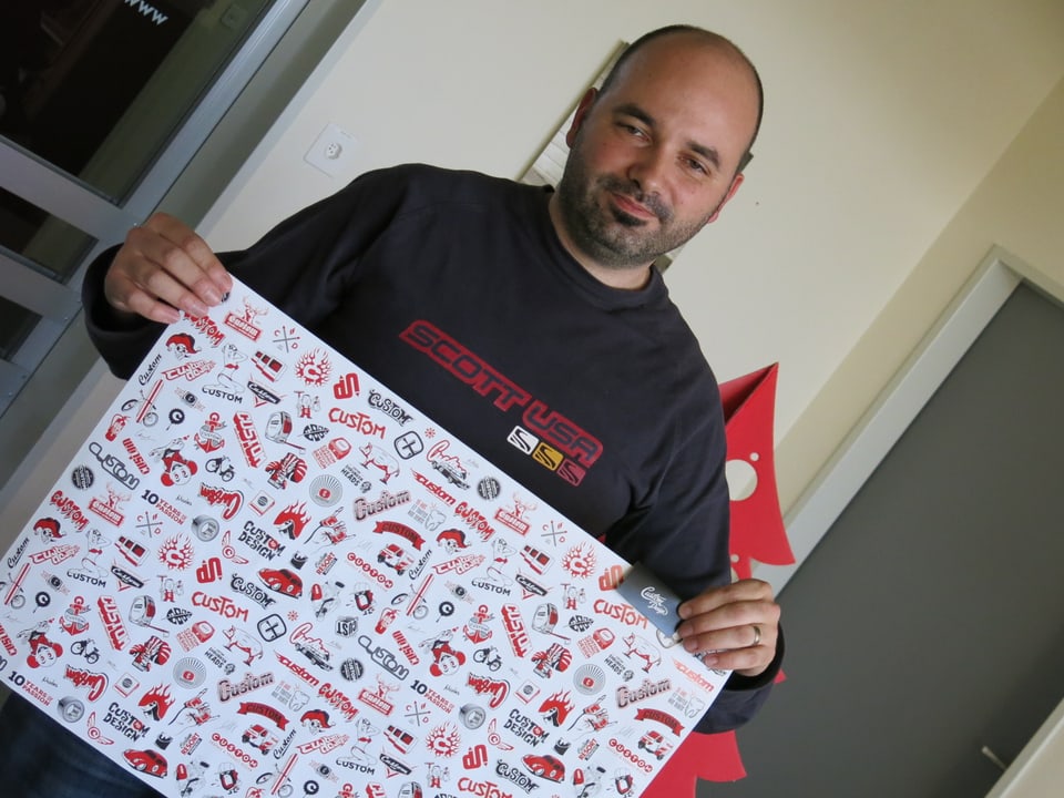 Laurent Kaeser hält ein Poster mit Logos der Firma Custom Design.