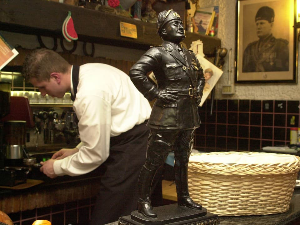 Die Bronzestatue des Duce steht auf dem Tresen, an der Wand ein Foto von Mussolini und im Hintergrund der Kellner an der Kaffeemaschine.
