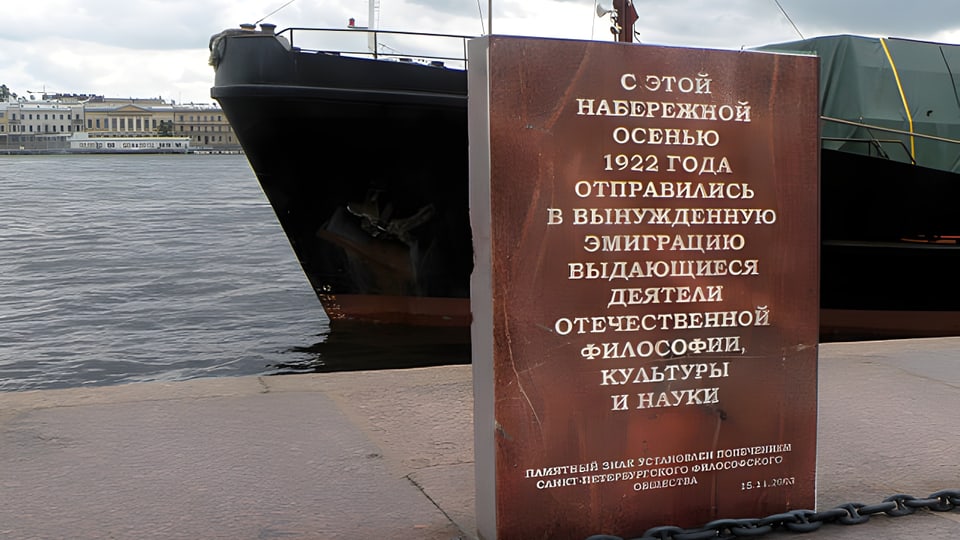Eine Tafel am Hafen mit russischen Namen. Dahinter sieht man den Bug eines Schiffes.