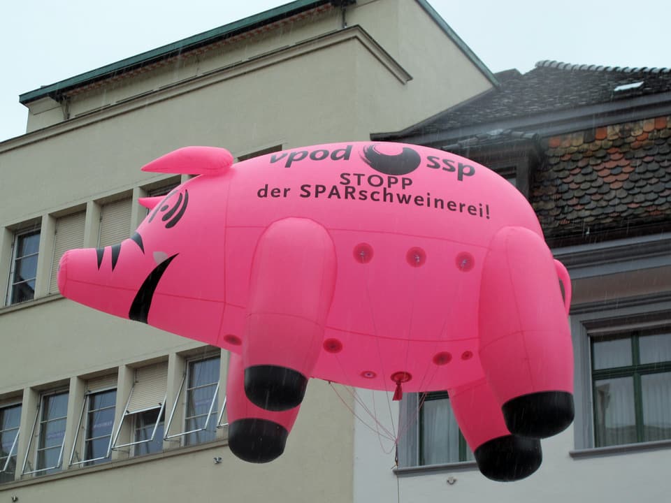 Ein rosarotes, aufblasbares Sparschwein fliegt mit der Aufschrift «Stopp der Sparschweinerei» durch die Luft.
