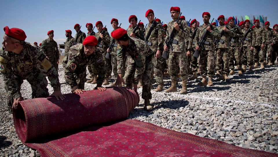 Soldaten rollen unter freiem Himmel einen roten Teppich aus.