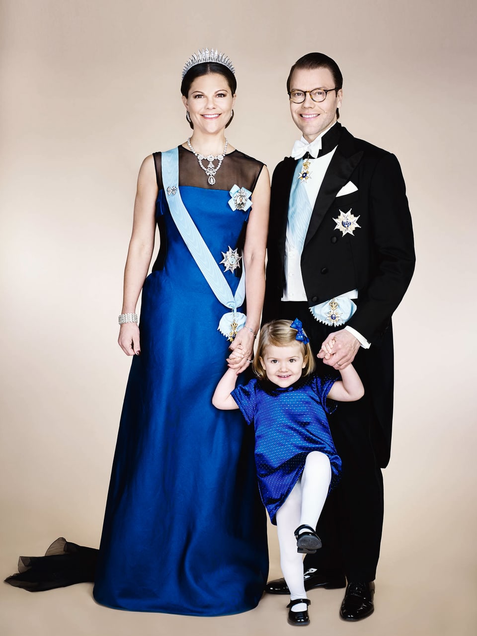 DIe Schwedischekranprinzenfamilie. Kronprinzessin Victoria im bodenlangen. blauen Kleid. Prinz Daniel trägt einen eleganten schwarzen Frack. Die kleine Etselle trägt auch ein blaues Kleid und will nicht so richtig stillstehen. 