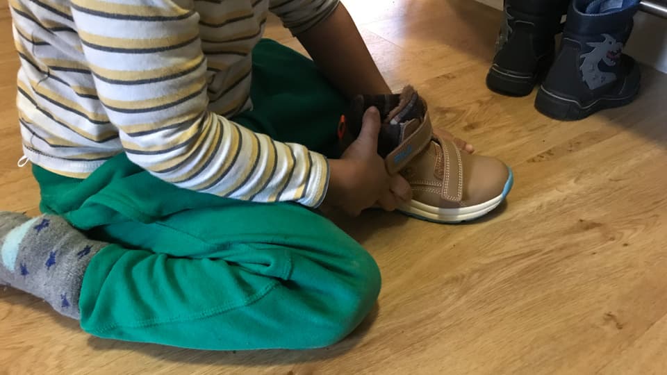 Ein Kind sitzt auf dem Boden und hält einen Schuh in der Hand. 
