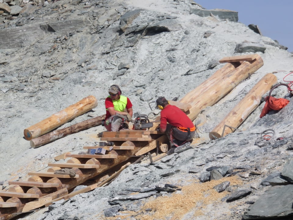 Zwei Arbeiter montieren eine Holztreppe in den Fels.
