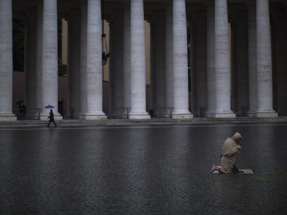 Barfüssiger Pilger im Bettelgewand kniend betend auf dem Petersplatz.