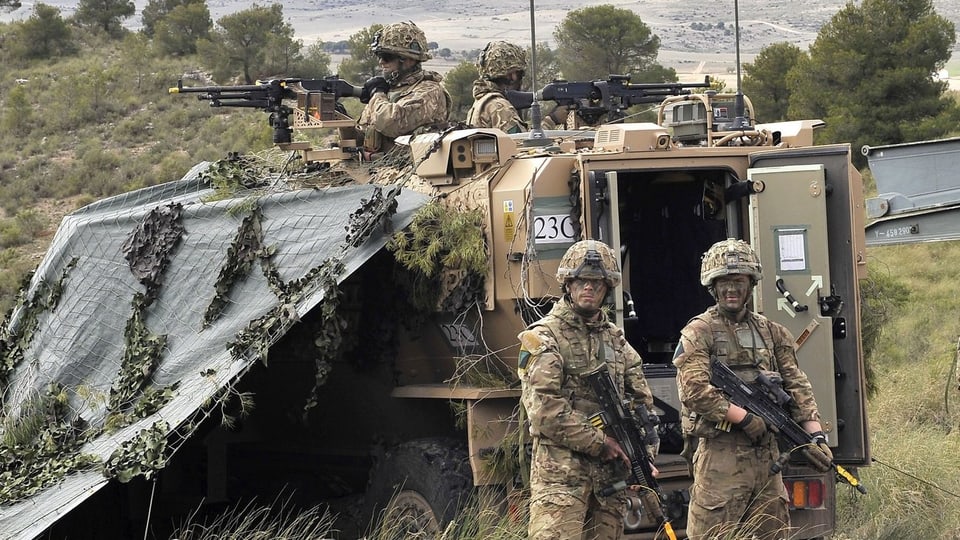 Bewaffnete Soldaten in Tarnanzügen stehen um ein gepanzertes Fahrzeug.
