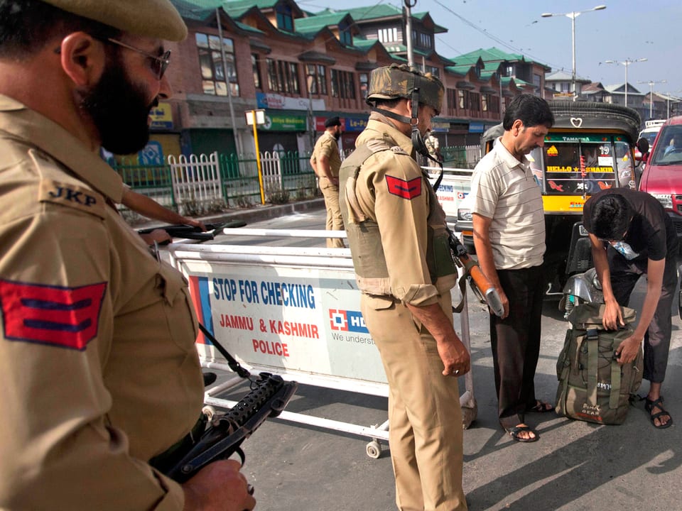 Indische Polizisten kontrollieren den Rucksack eines Passanten.