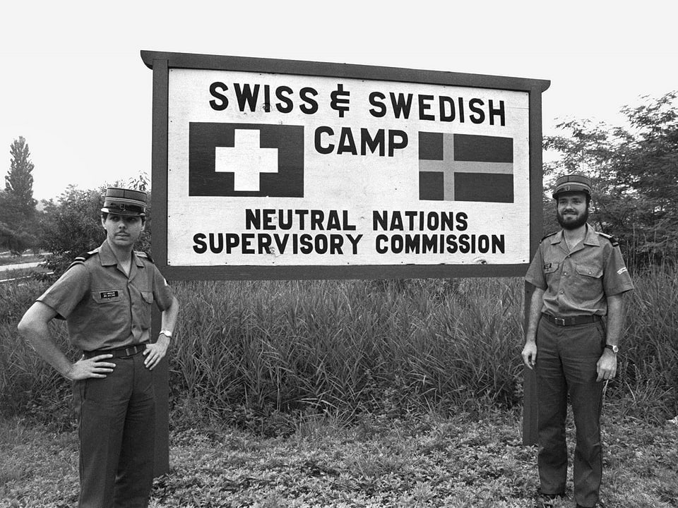 Zwei Soldaten stehen vor einem Schild mit der Aufschrift «Swiss & Swedish camp».