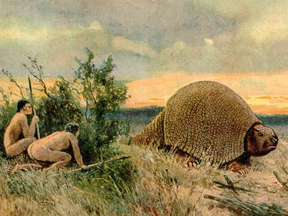 Zwei Menschen hocken hinter einem Buch und lauern einem Glyptodon auf. 