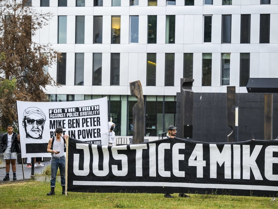 Männer stehen mit Bannern vor einem Gebäude. Auf einem Banner steht «Justice 4 Mike».