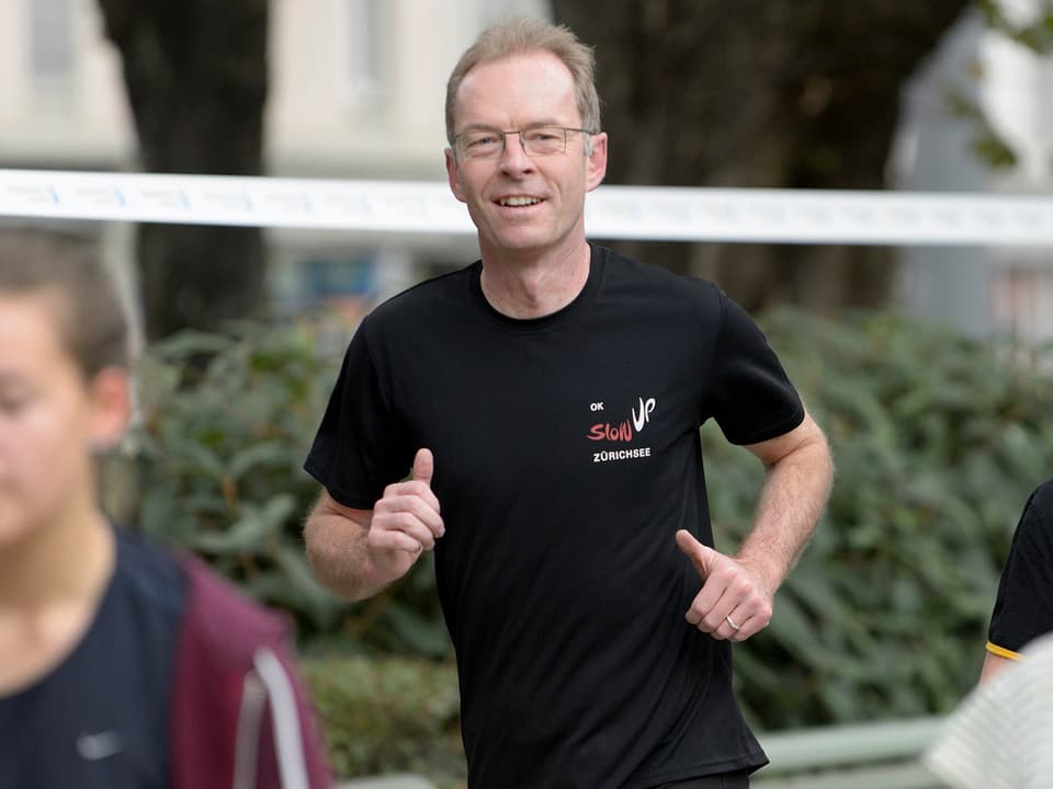 Ein Mann mit Brille in schwarzem T-Shirt rennt durch einen Park. 