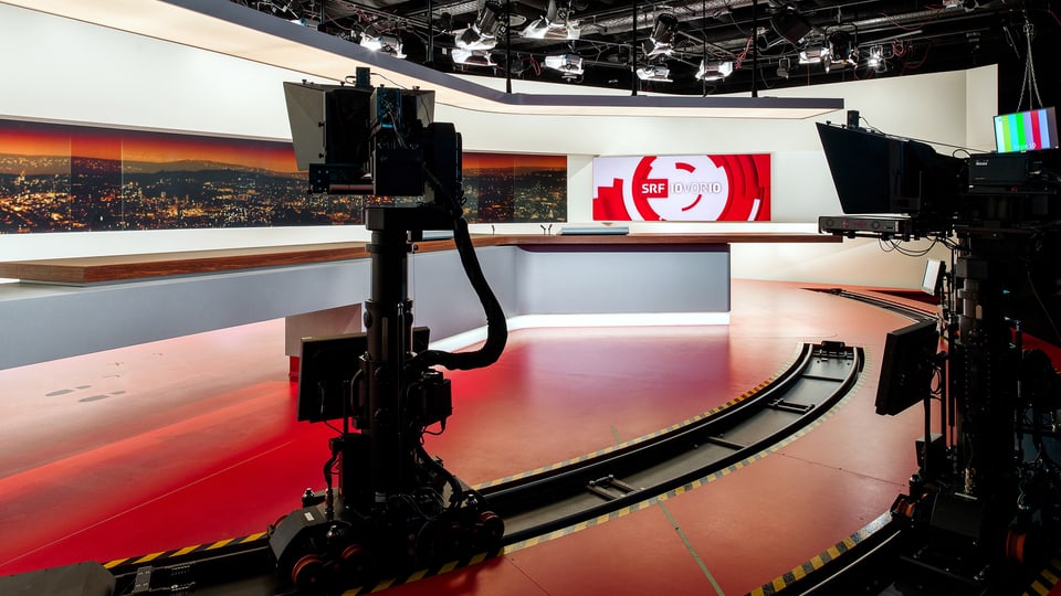 Blick ins 10vor10-Studio: Im Vordergrund sieht man eine automatisierte Kamera auf Schienen, im Hintergrund das Moderationspult sowie das Logo von 10vor10 auf einem Bildschirm rechts und links die Skyline bei Nacht. 