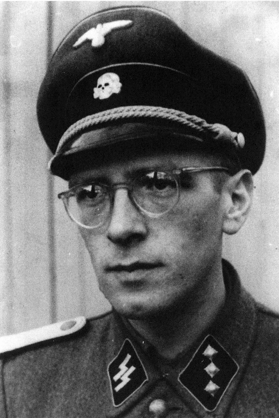 Schwarzweissfoto: Ein Mann mit Brille in Uniform: Am Kragen sind die Runen der SS zu sehen, am Hut das Totenkopf-Symbol.