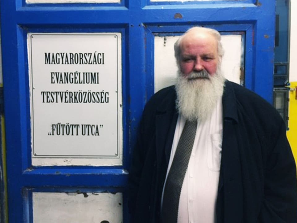 Gábor Iványi mit langem, weissem Bart vor einer Türe. 