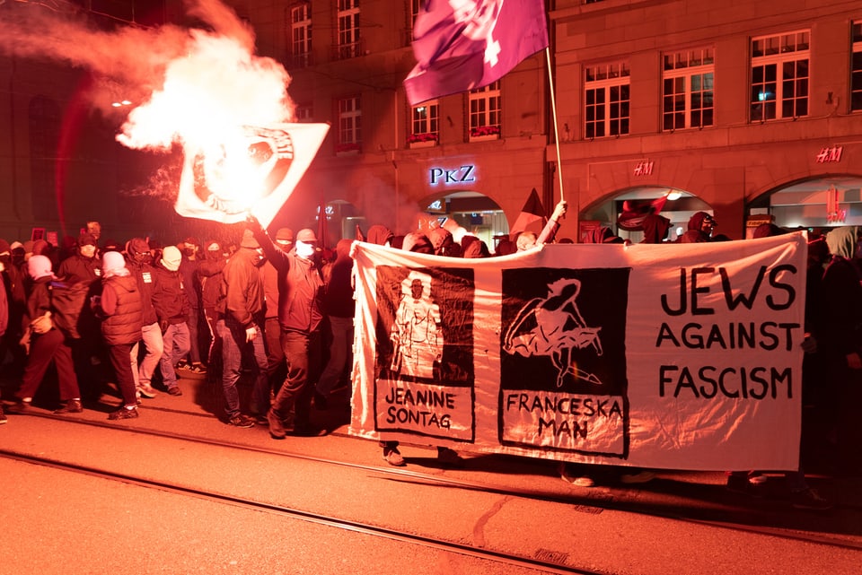 Kundgebende in der Stadt Bern, mit Feuer und Plakaten. Einige davon sind vermummt.