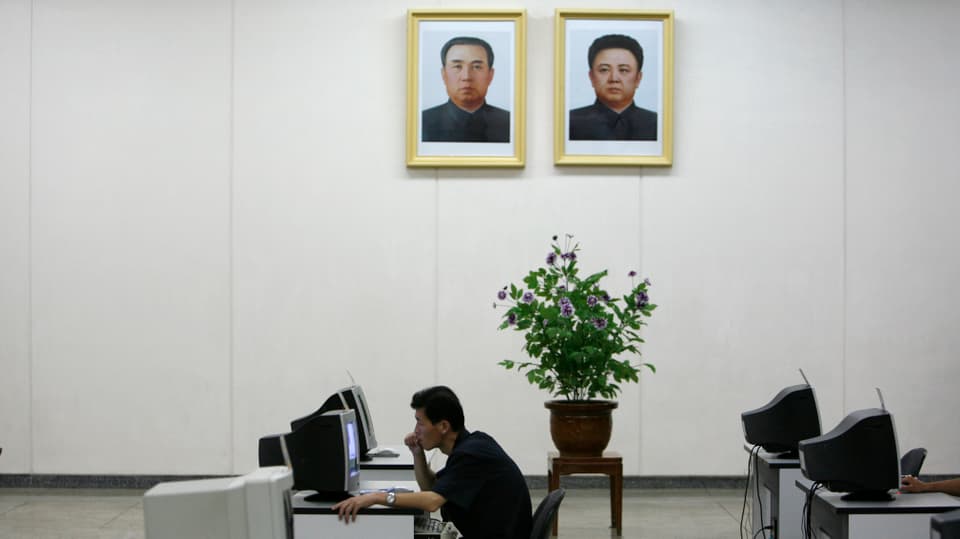 Ein Nordkoreaner sitzt an einem Computer, über ihm an die Wand gehängt ein Portrait von Kim Il-sun und Kim Jong-il.