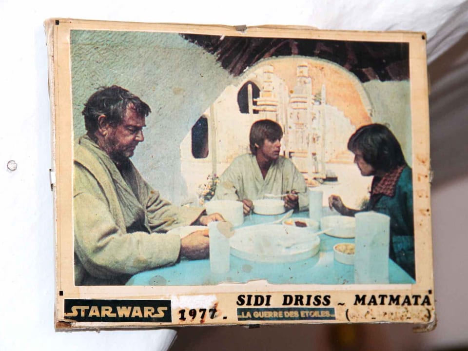 Altes Foto mit drei Personen am Tisch in einer Art Höhle. 