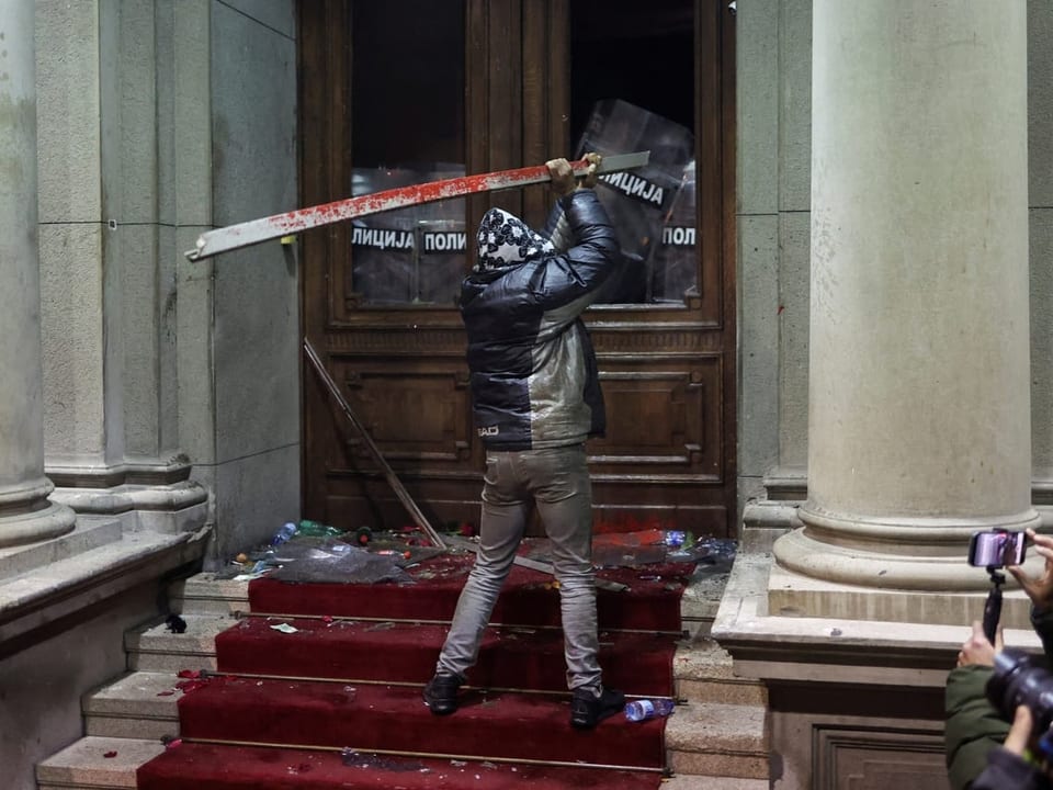 Ein Mann schlägt mit einer Metallstange auf den Eingang des Belgrader Rathauses ein.