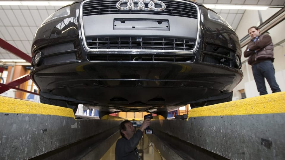 Audi auf Prüfstand, Mechaniker im Untergrund leuchtet mit Taschenlampe den Unterboden