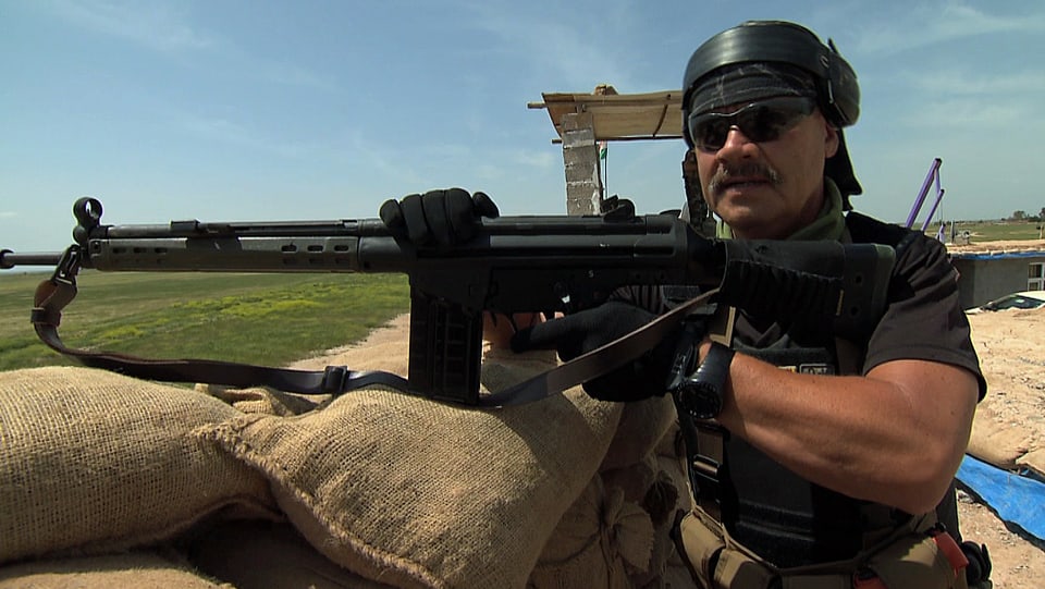 Ein Mann mit T-Shirt und Sturmgewehr auf einem Beobachtungsposten.