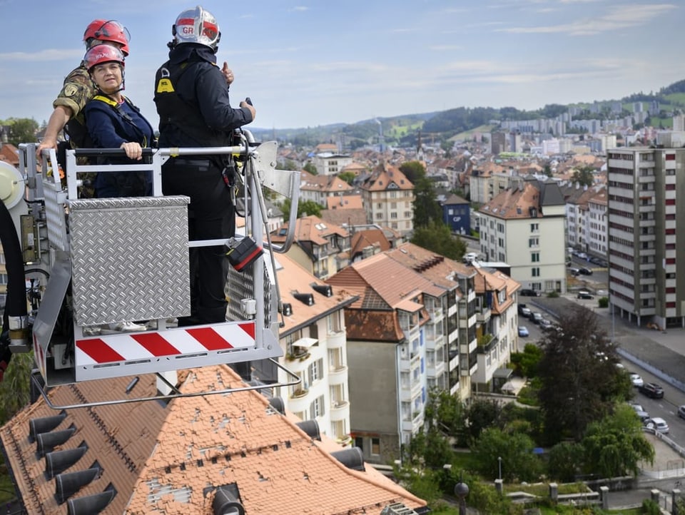 Viola Amherd mit Feuerwehrleuten auf einem Kran über den Dächern der Stadt
