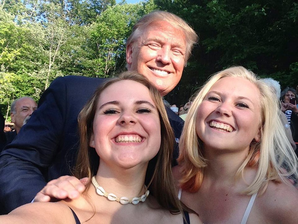 Trump posiert mit zwei jungen Frauen für ein Selfie.