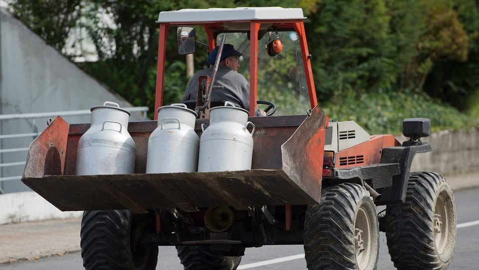 Ein Bauer transportiert Milchkannen mit dem Traktor.