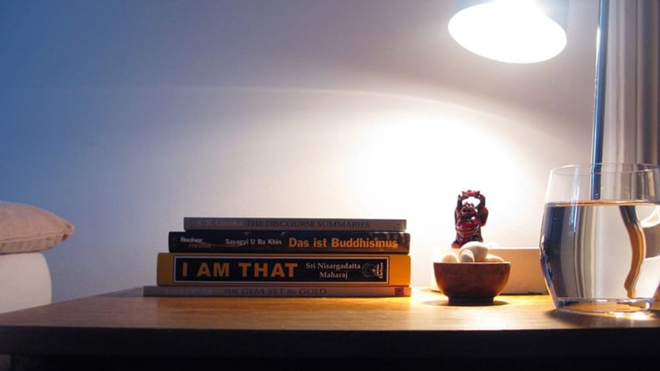 Auf einem Nachttisch stehen eine  kleine Buddha-Statue und buddhistische Bücher