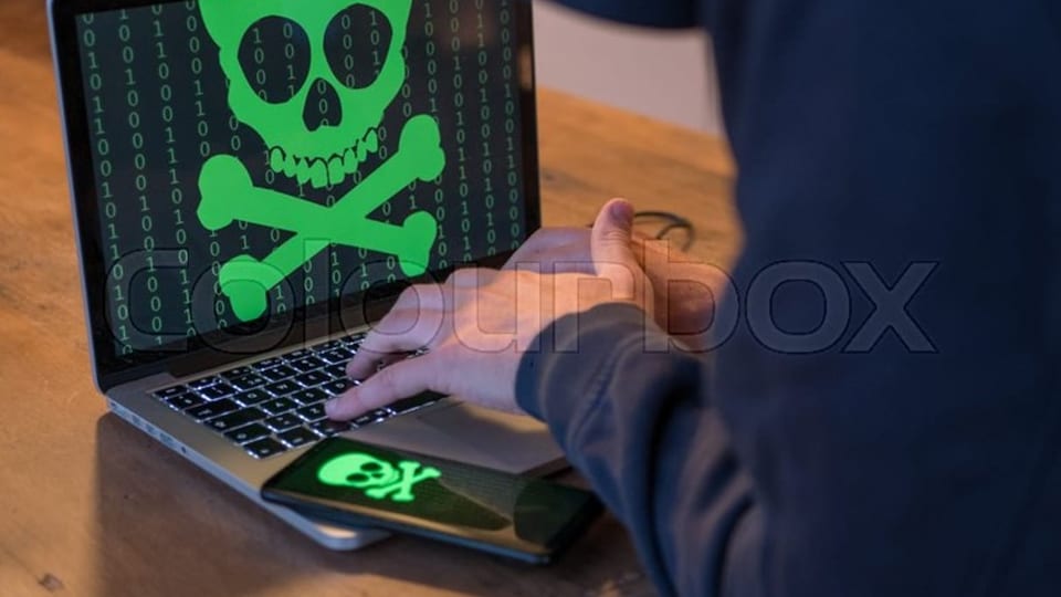 Ein Hacker sitzt vor einem Laptop, auf dem ein grüner Totenkopf zu sehen ist.