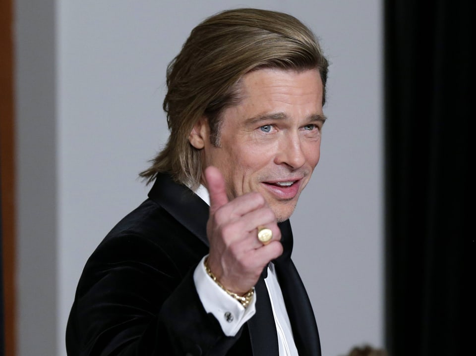 Brad Pitt hebt die Hand und den Daumen.