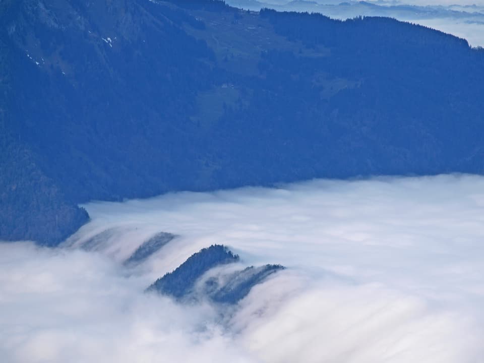 Grauer Hochnebel fliesst wie ein Wasserfall über einen Berg.