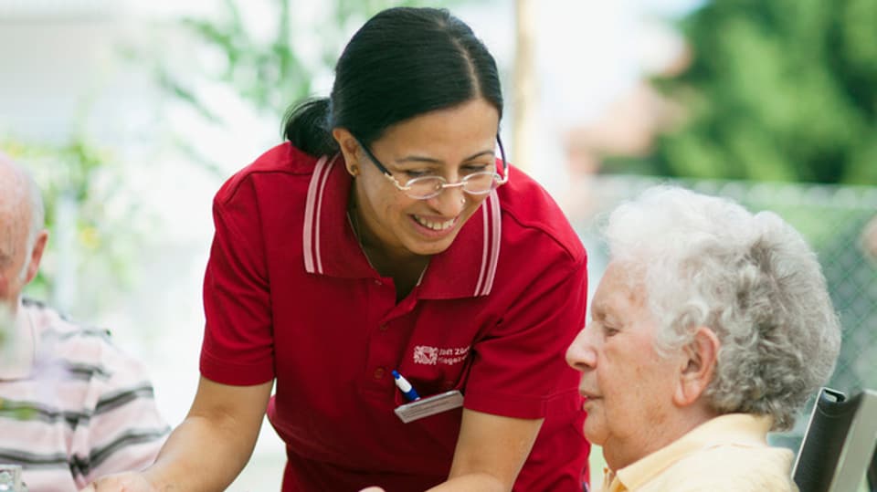 Eine Pflegerin wendet sich lächelnd einer Seniorin zu.
